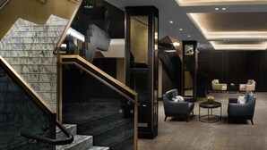 A modern interior with a marble staircase, a glass elevator, and a seating area with sofas and a coffee table. - Hilton London Bankside (London)