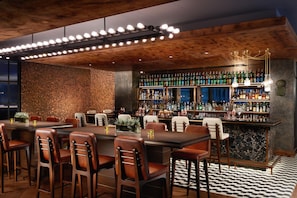 A bar area with a long counter, multiple chairs, and a variety of bottles. - Hilton London Bankside (London)