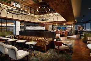 A bar area with leather seating, round tables, and a bar counter with bottles. - Hilton London Bankside (London)