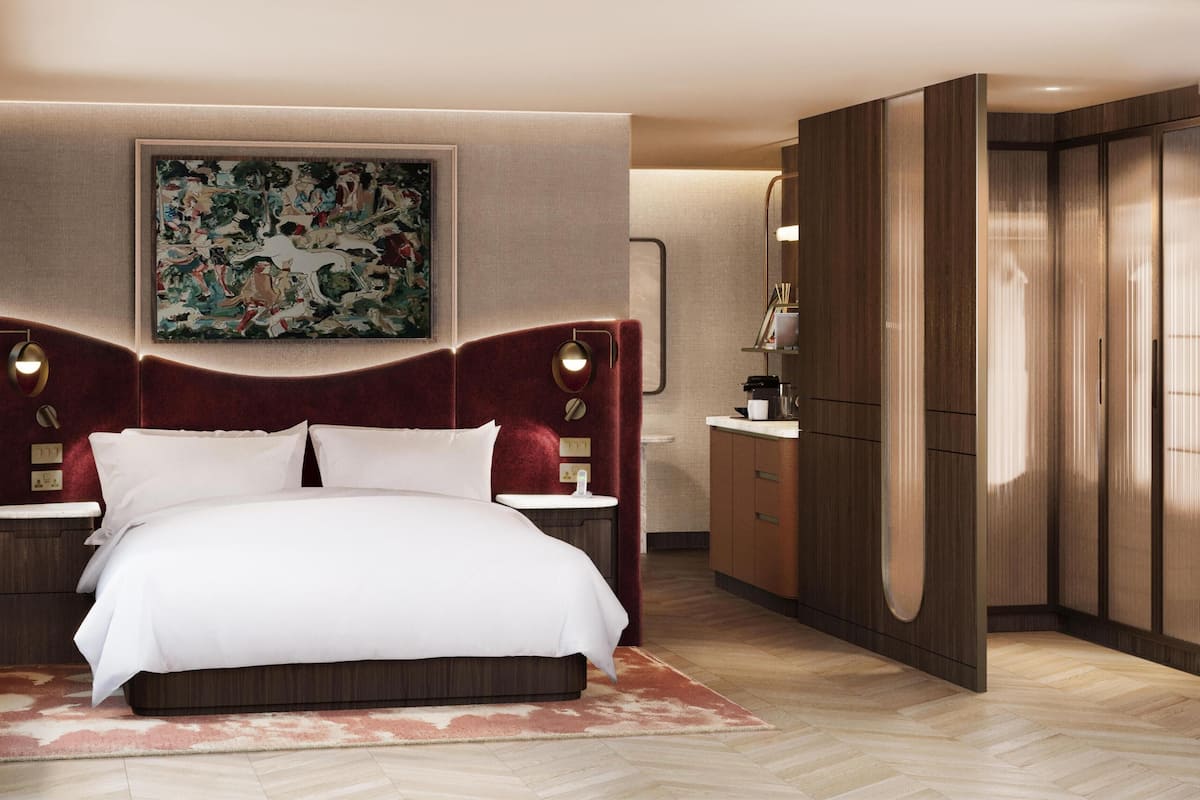 Habitación de hotel con una cama grande, un cuadro en la pared, un armario y una mesita de noche con lámpara.