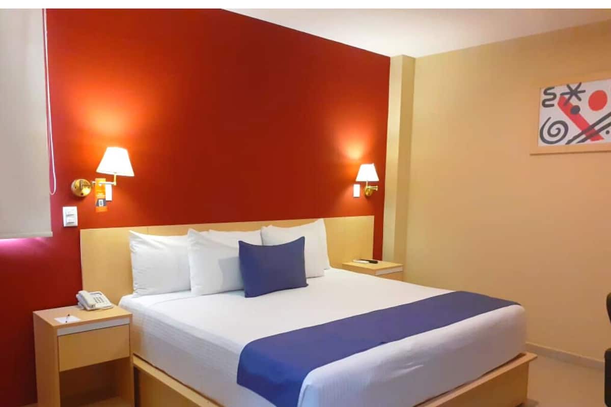 A hotel room with a large bed, two bedside lamps, a nightstand with a phone, and a wall-mounted artwork.