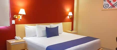 A hotel room with a large bed, two bedside lamps, a nightstand with a phone, and a wall-mounted artwork.
