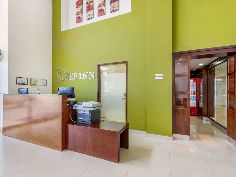 A reception desk with a sign reading "SLEEPPINN" in a modern lobby with green walls and a glass door leading to a reception area.