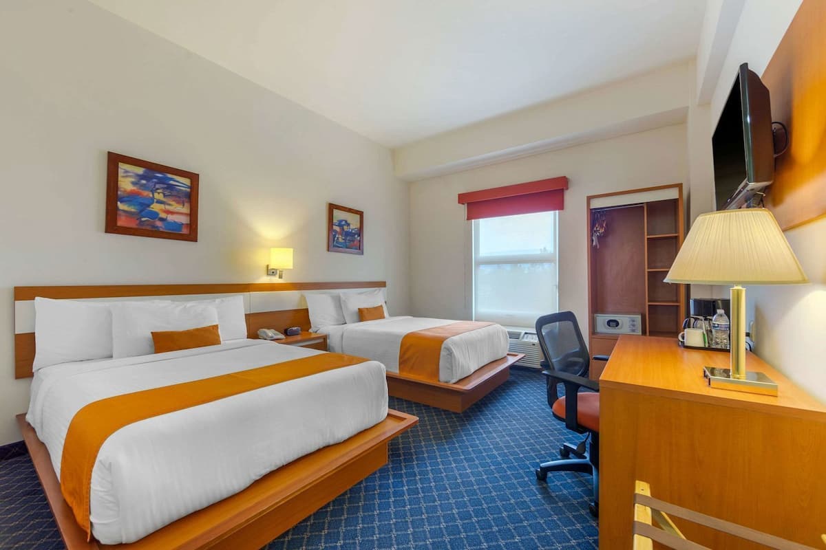 A hotel room with two beds, a desk, a chair, a TV, and artwork on the walls.
