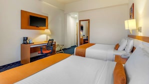 A hotel room with two beds, a desk with a chair, a television, and a lamp.