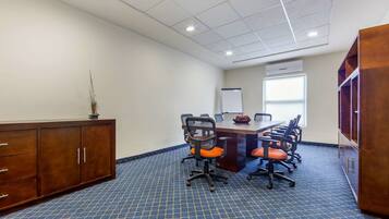 Uma sala de conferência com uma mesa grande, seis cadeiras de escritório, um quadro branco e uma janela.