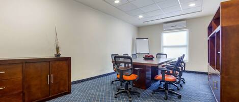 Uma sala de conferência com uma mesa grande, seis cadeiras de escritório, um quadro branco e uma janela.