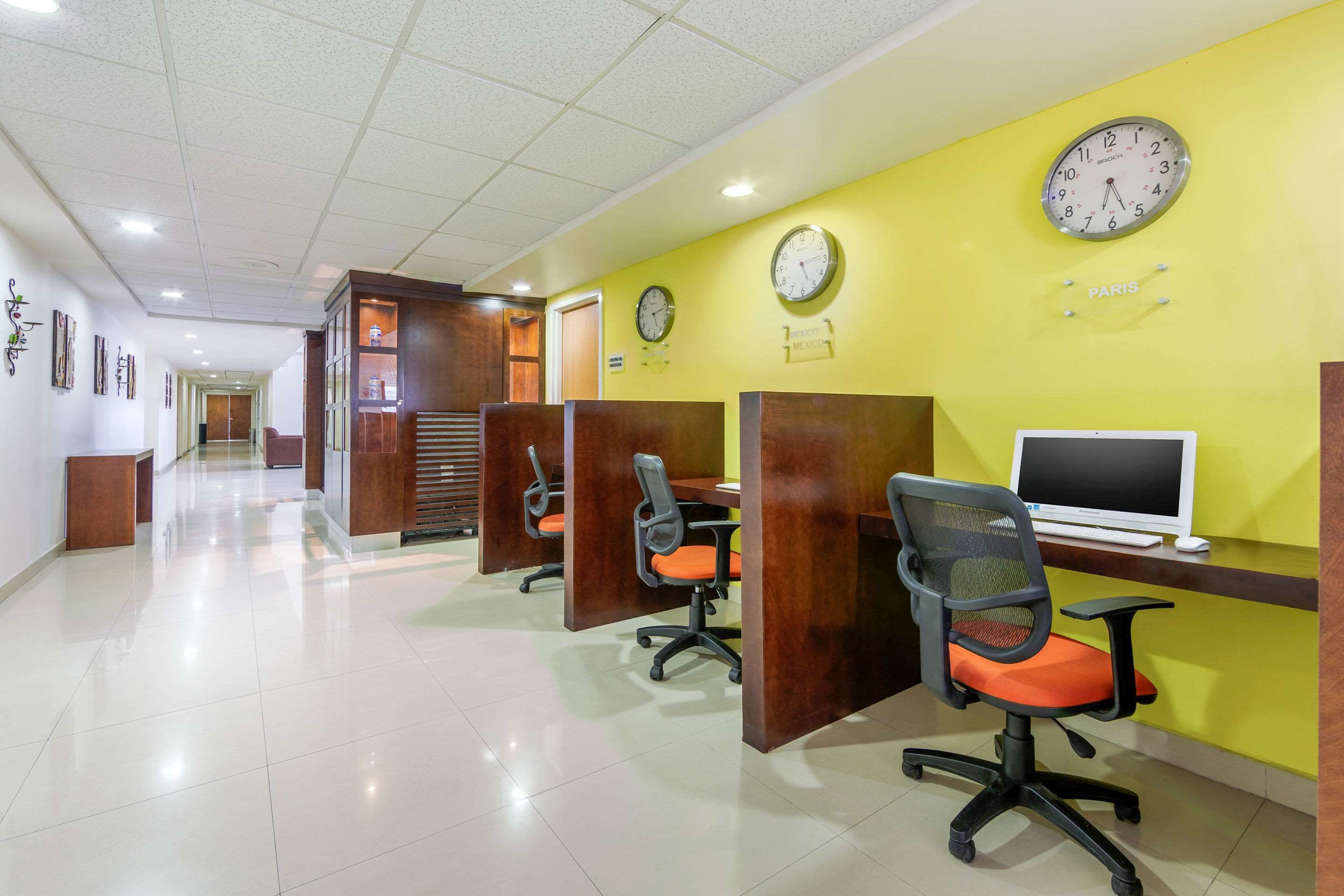 A modern office space with cubicles, computers, and clocks on the wall.
