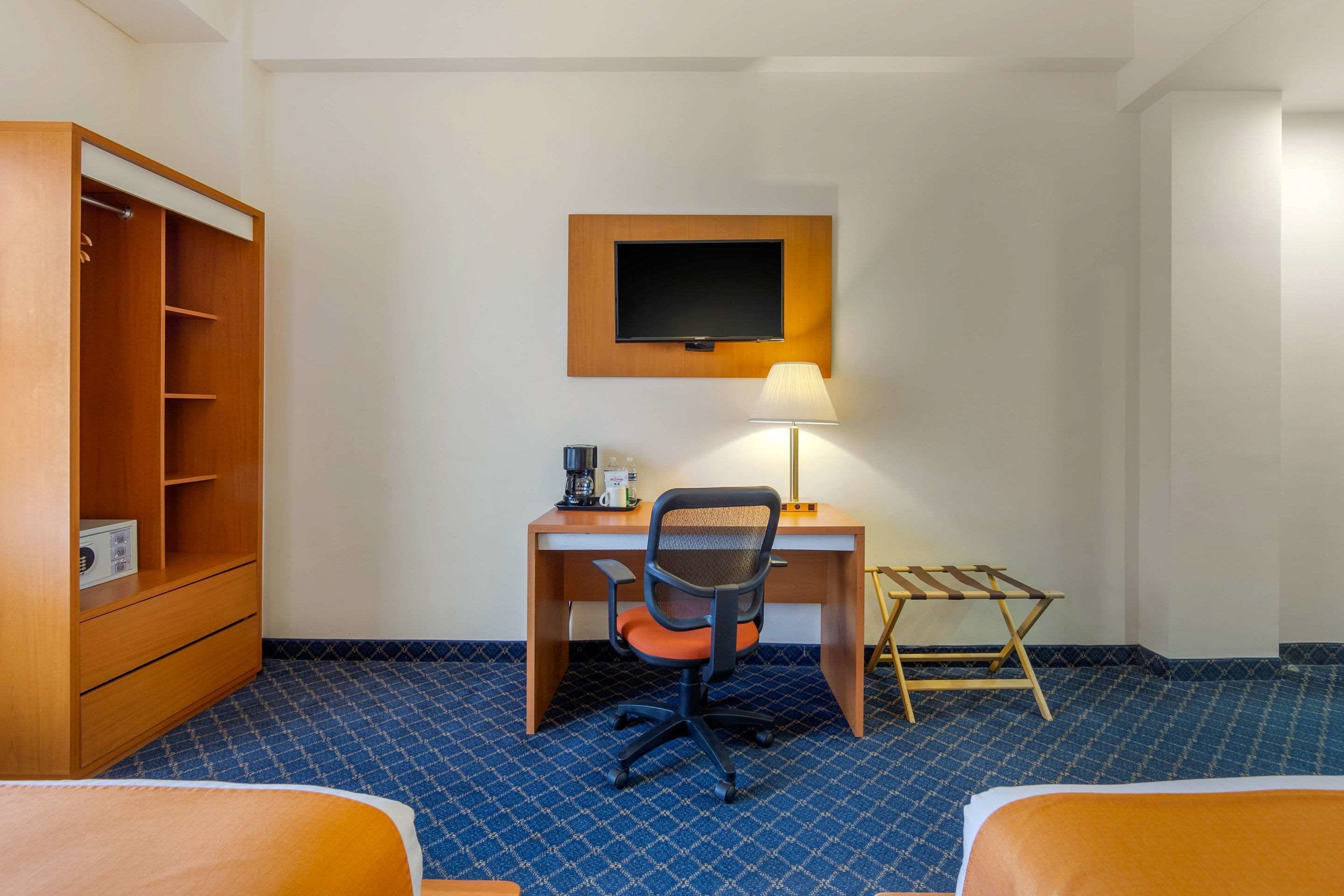 Ein Hotelzimmer mit einem Bett, einem Schreibtisch mit Stuhl, einem an der Wand montierten Fernseher und einem Kleiderschrank.