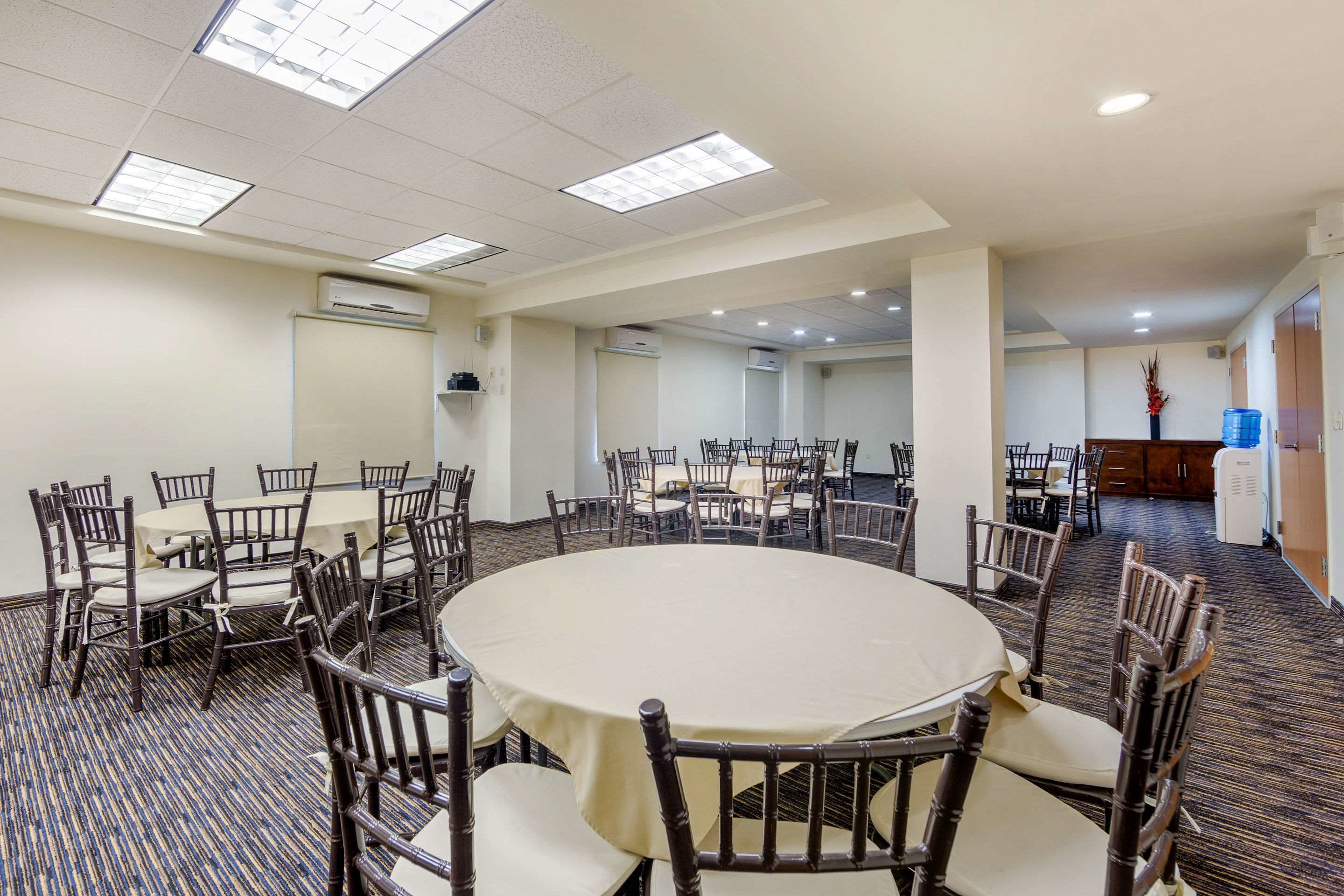 A conference room with round tables and chairs, air conditioning units, and a water dispenser.