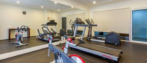 A gym with various cardio machines, a mirrored wall, and a door to a changing room.
