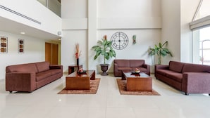 A spacious lobby with a high ceiling, two sofas, three coffee tables, and large potted plants.