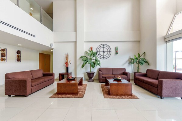 A spacious lobby with a high ceiling, two sofas, three coffee tables, and large potted plants.