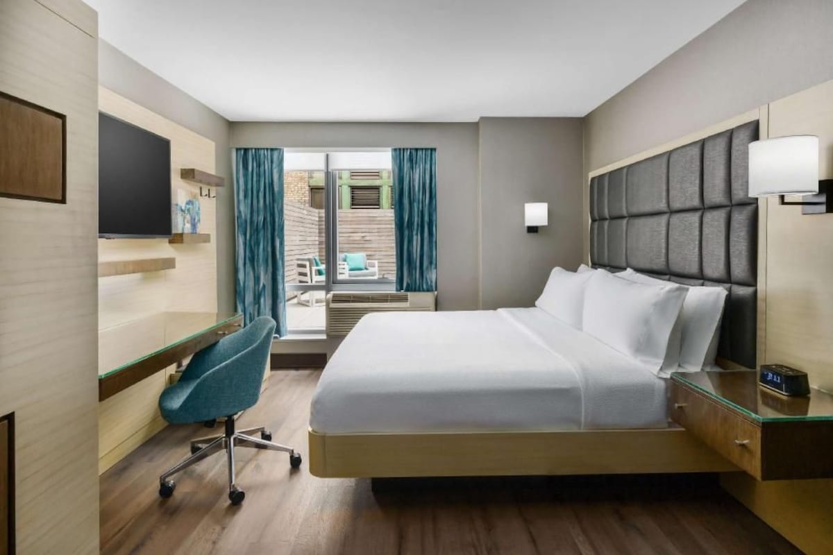Une chambre d’hôtel équipée d’un lit, d’un bureau, d’une chaise, d’une télévision et offrant une vue sur l’extérieur.