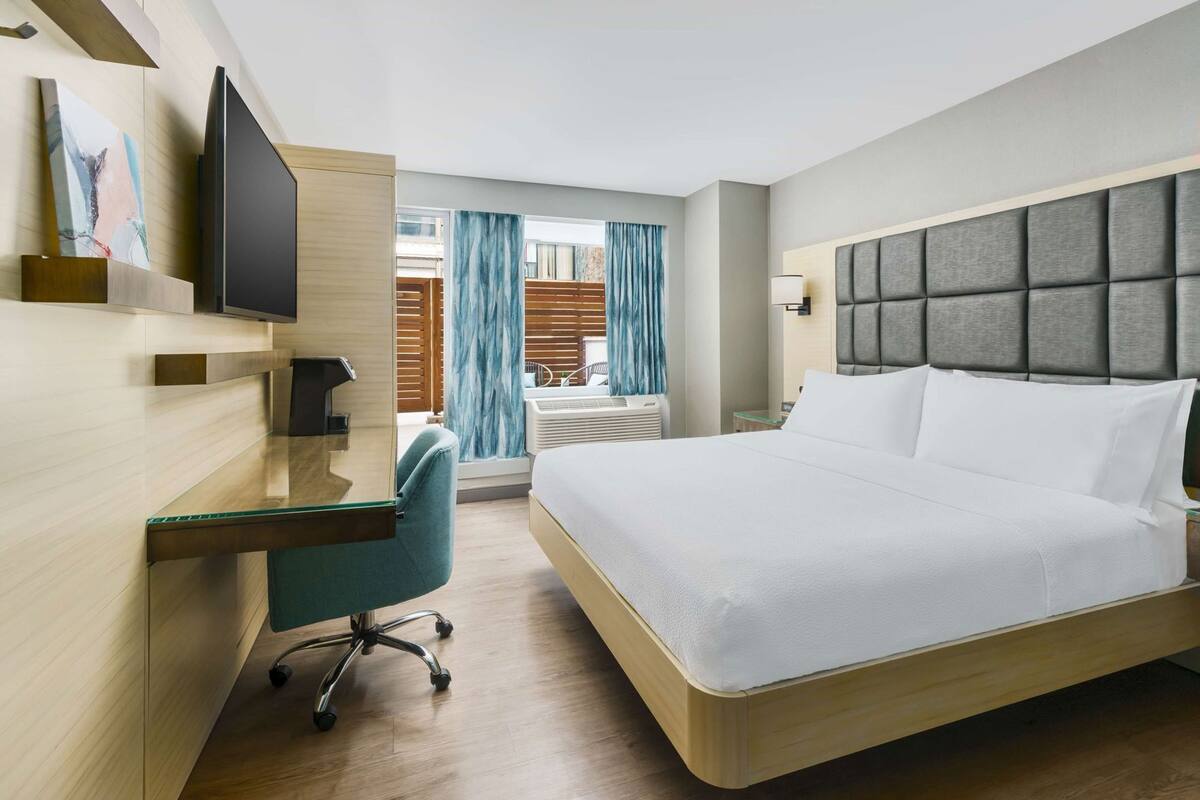 Habitación de hotel con cama, escritorio, silla, televisión y ventana con cortinas.