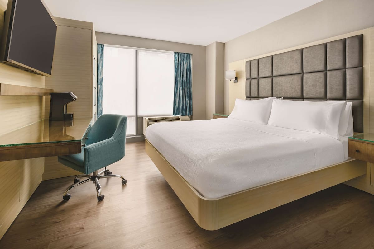 Une chambre d’hôtel avec un grand lit, un bureau avec une chaise, un téléviseur à écran plat et une fenêtre avec des rideaux.