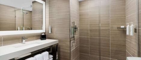 A modern bathroom with a large mirror, a sink, a shower, and a toilet.