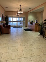 A hotel lobby with a reception desk, seating area, and a view through the glass doors.