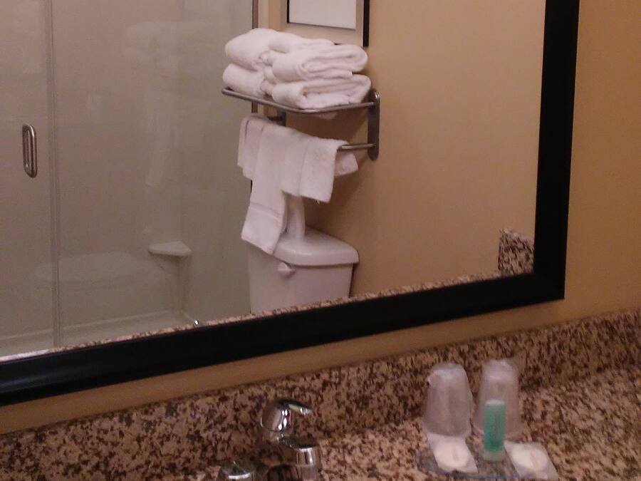 A bathroom with a large mirror, a sink, and a towel rack with folded towels.