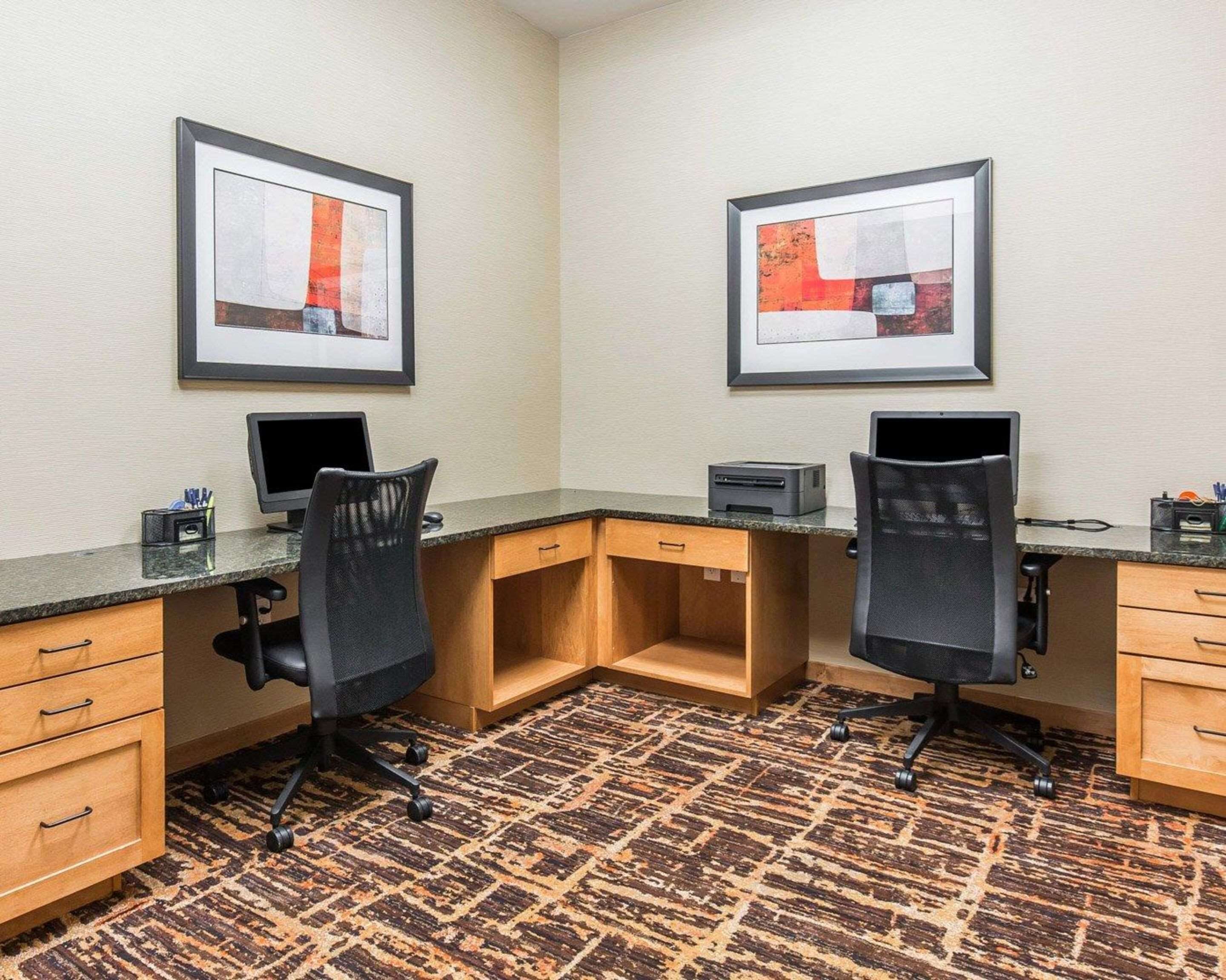 Habitación de hotel con dos escritorios, cada uno con una computadora e impresora, y piso cubierto de alfombra.