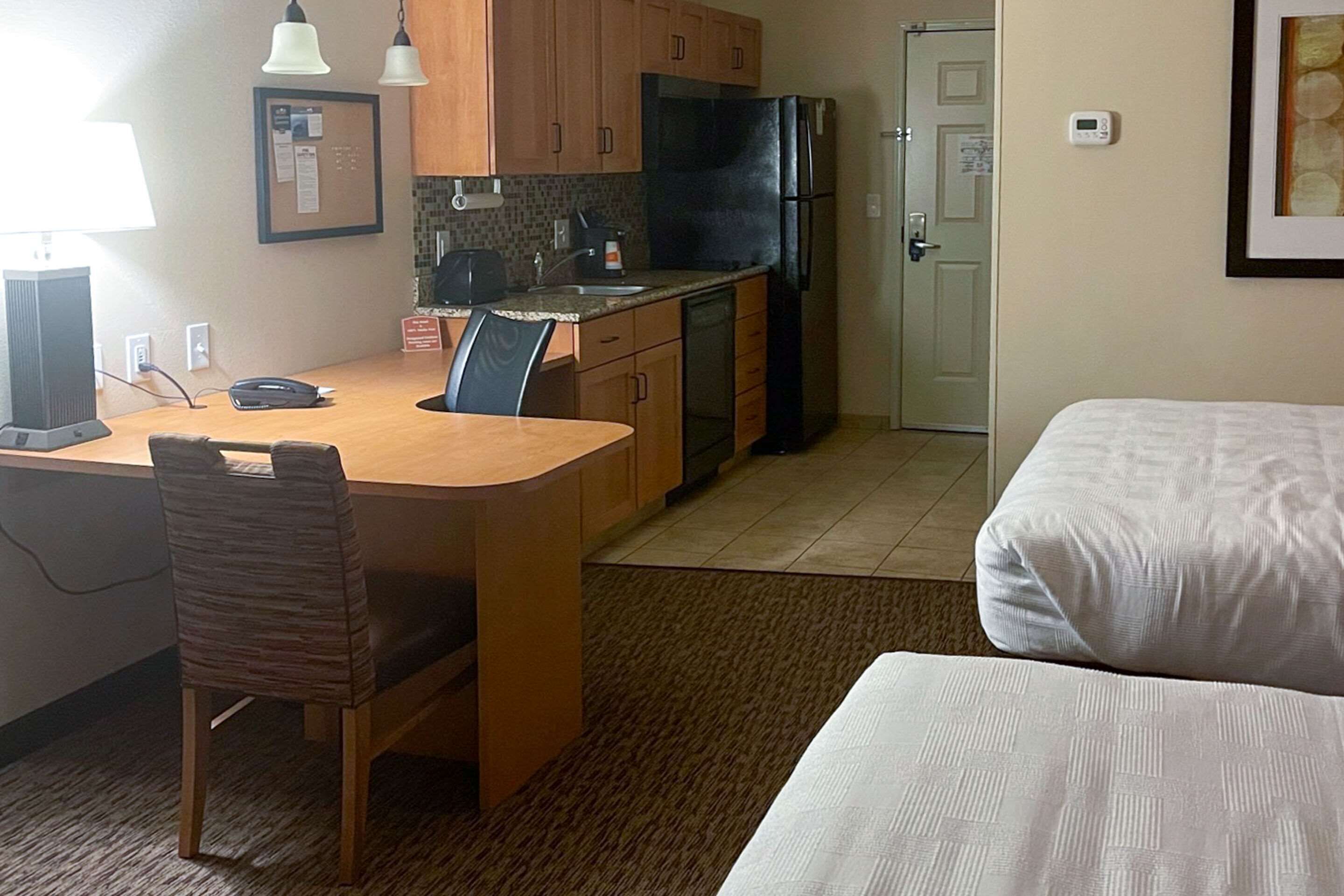 A compact hotel room with a kitchenette, a dining area with a chair and table, and a bed.