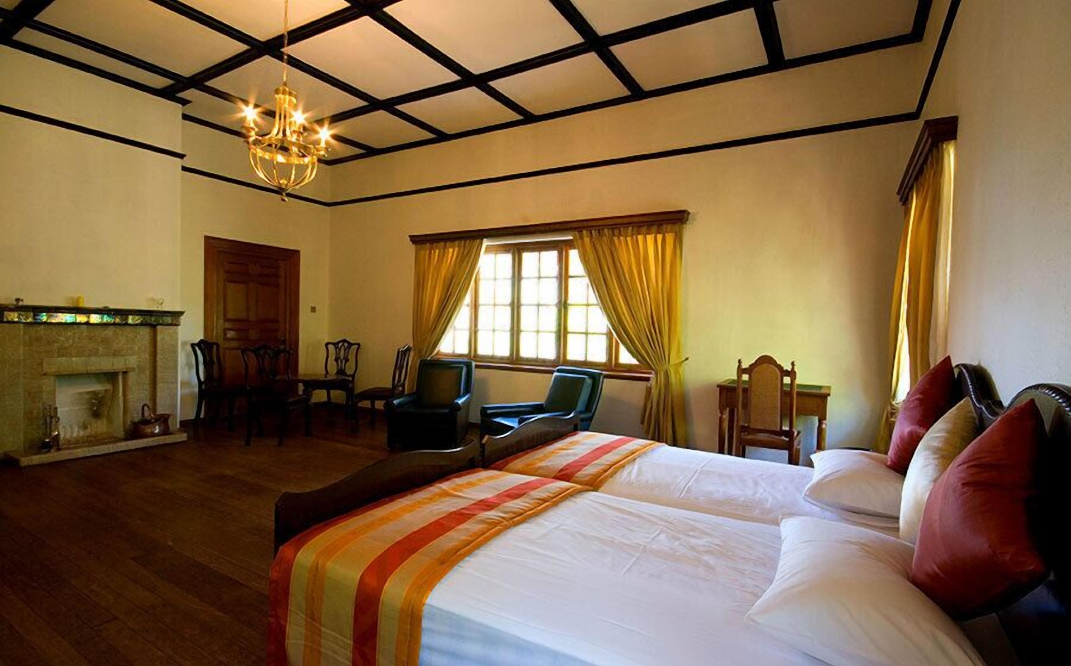 A hotel room with a large bed, a fireplace, a chandelier, and a view of the outdoors through a window with curtains.
