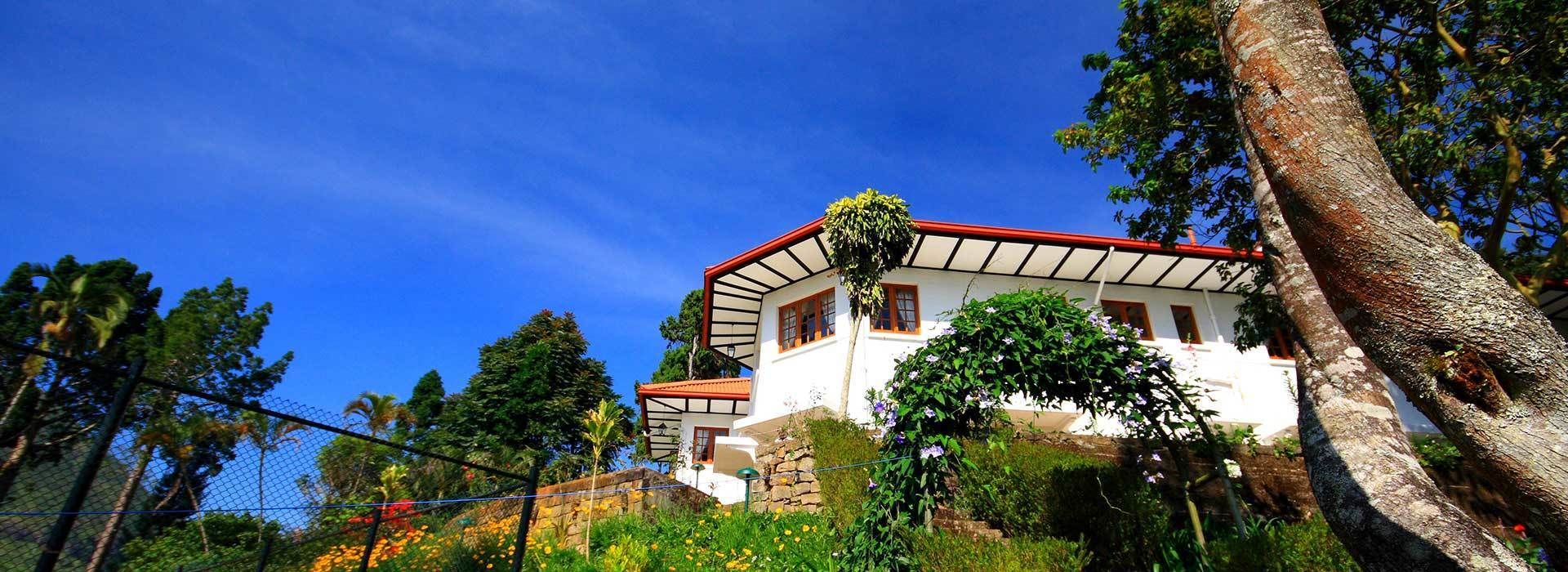 Um edifício branco com telhado vermelho, rodeado por vegetação e árvores.