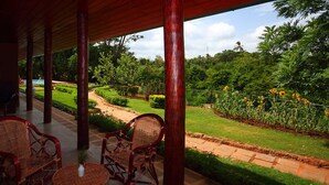 A covered outdoor area with wicker furniture and a view of a landscaped garden. - Governor's Gangula (Dambulla)