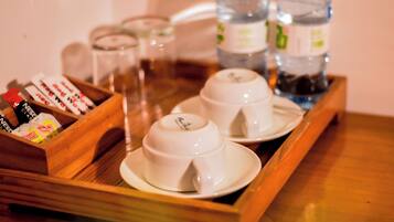 Una bandeja con dos tazas y platillos blancos, una caja de madera con varios objetos y botellas de agua.