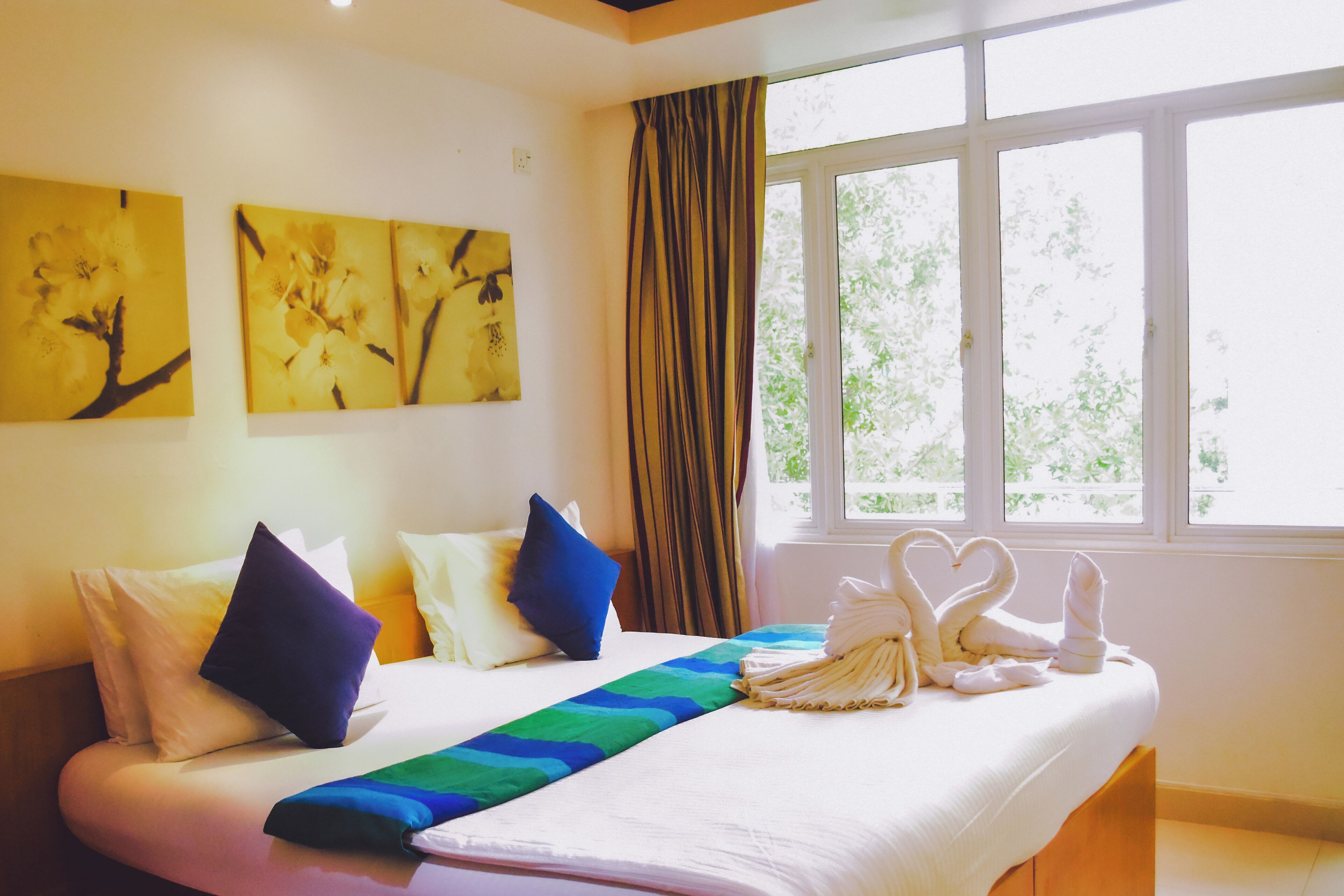A hotel room with a bed, pillows, a blanket, and wall art.
