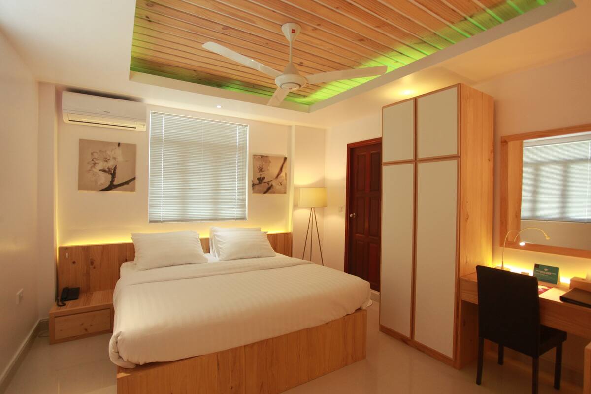 A bedroom with a bed, bedside table, lamp, desk, chair, wardrobe, and ceiling fan.