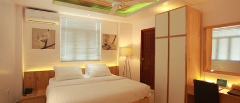A bedroom with a bed, bedside table, lamp, desk, chair, wardrobe, and ceiling fan.