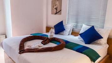 Una cama bien hecha con una disposición de toallas en forma de corazón, almohadas azules y blancas, y una manta a rayas azules y verdes.