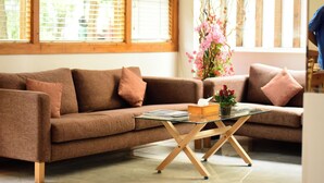 A living room with a brown sofa, a glass coffee table, and a vase with flowers. - Pine Lodge Maldives (Hulhumalé)