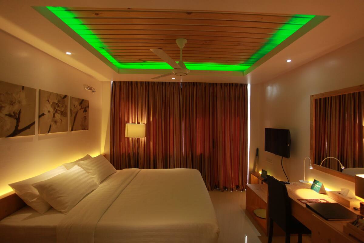 A hotel room with a bed, desk, chair, lamp, and a television.