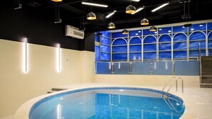 A swimming pool with a tiled edge, a metal ladder, and a blue-tiled wall with arched windows in the background. - Saraya Corniche Hotel (Doha)