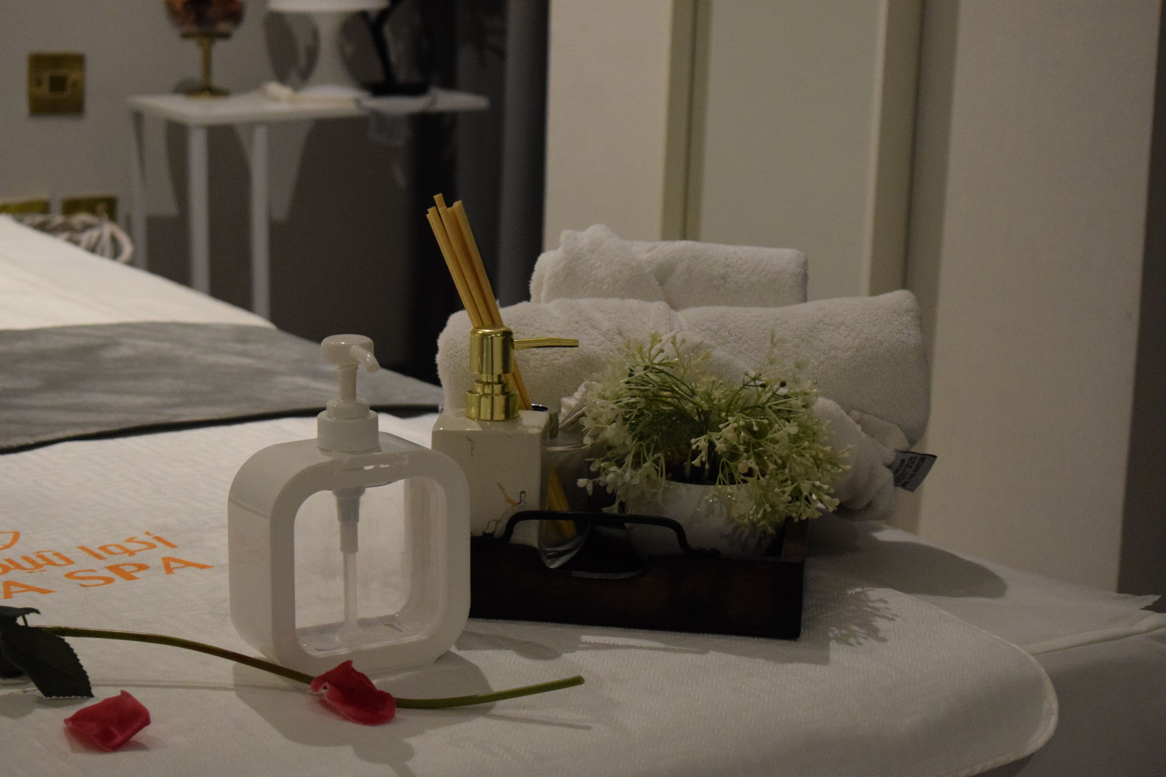 A neatly arranged spa bed with a bottle of lotion, a small potted plant, and a pair of glasses.