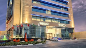 A tall hotel with multiple floors, large windows, and a well-lit entrance. - Saraya Corniche Hotel (Doha)