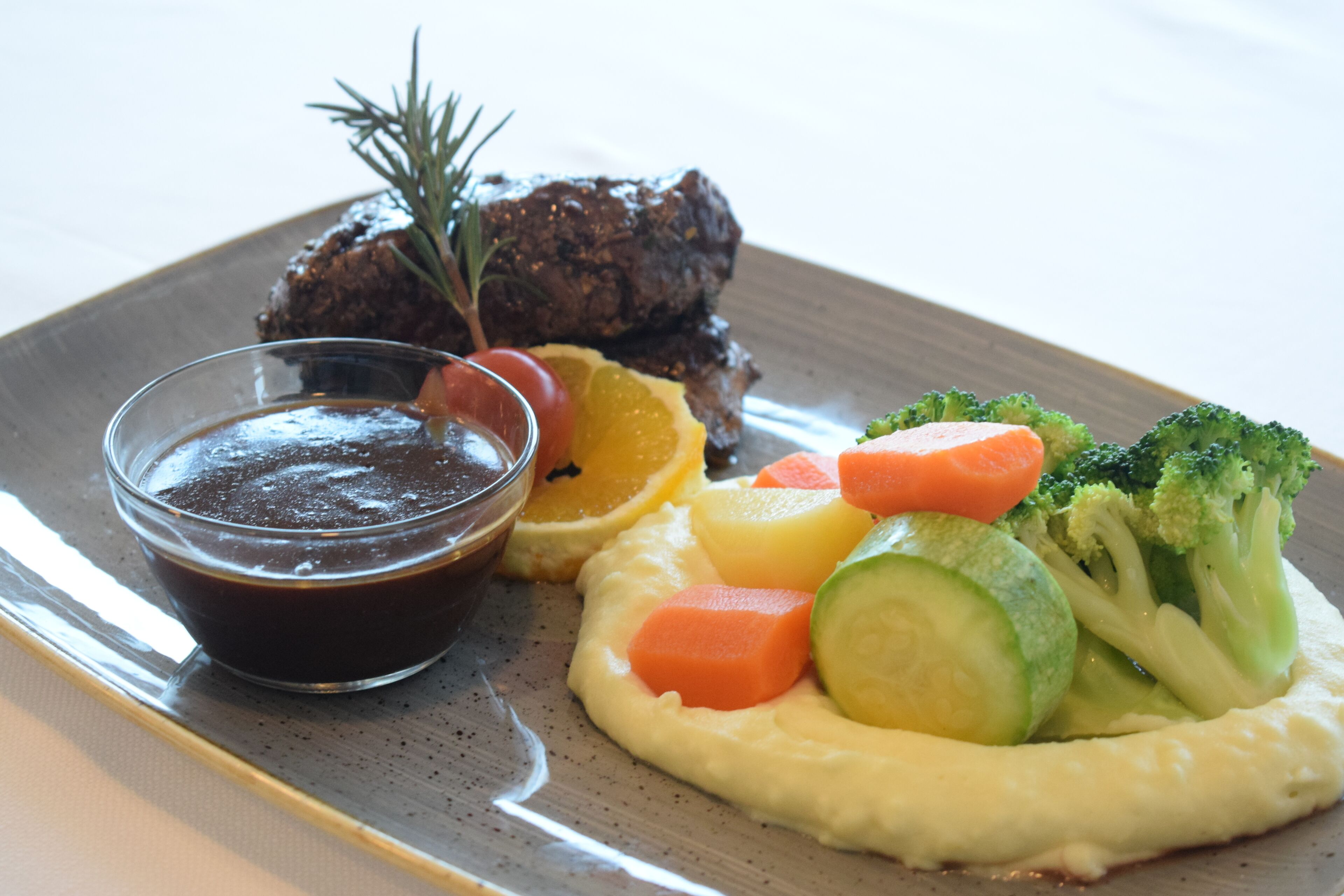 Um prato com bife, legumes e molho.