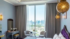 A hotel room with a bed, two chairs, a desk, a mirror, and a large window with a city view. - Saraya Corniche Hotel (Doha)