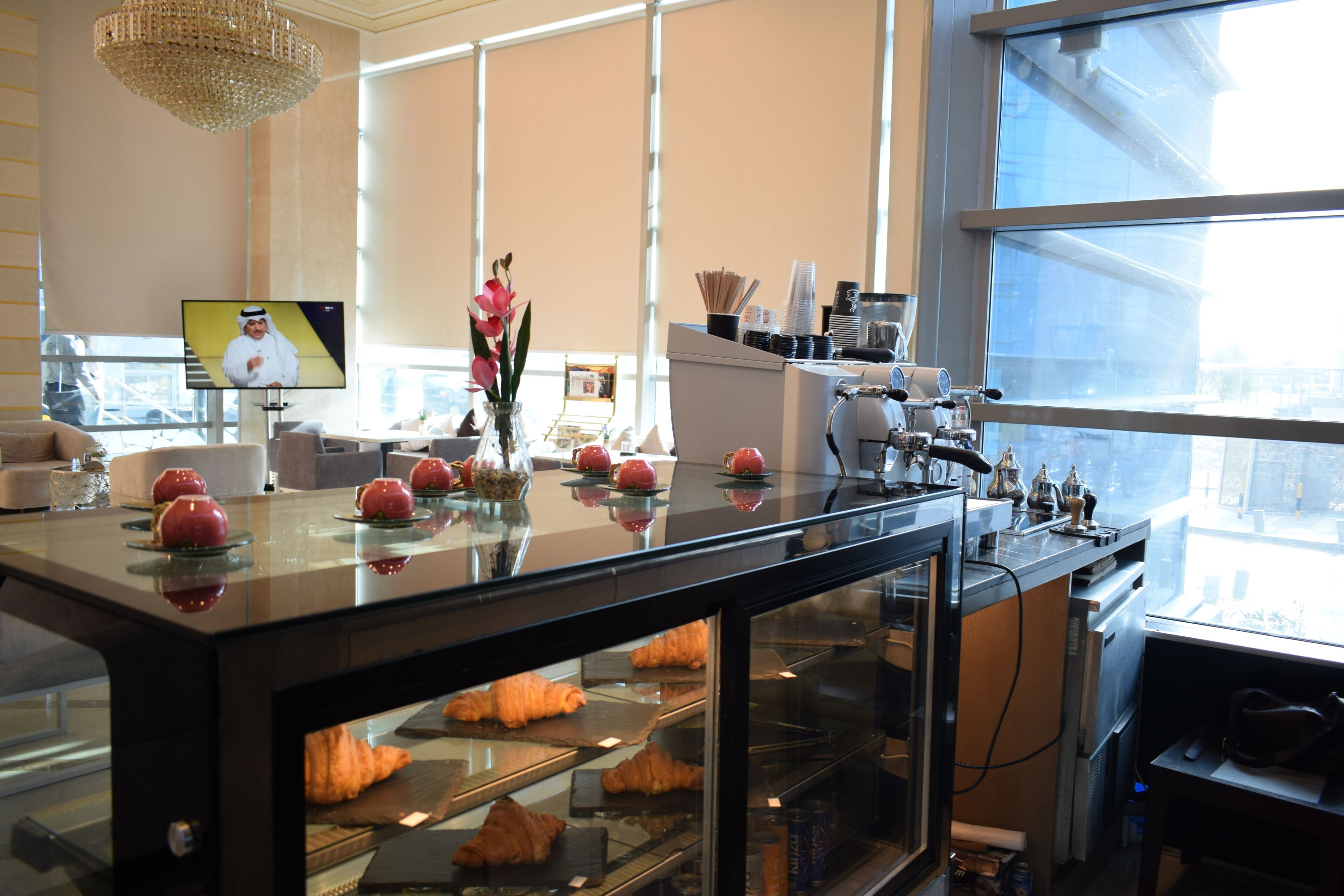 A bakery counter with pastries, a television, and a large window.