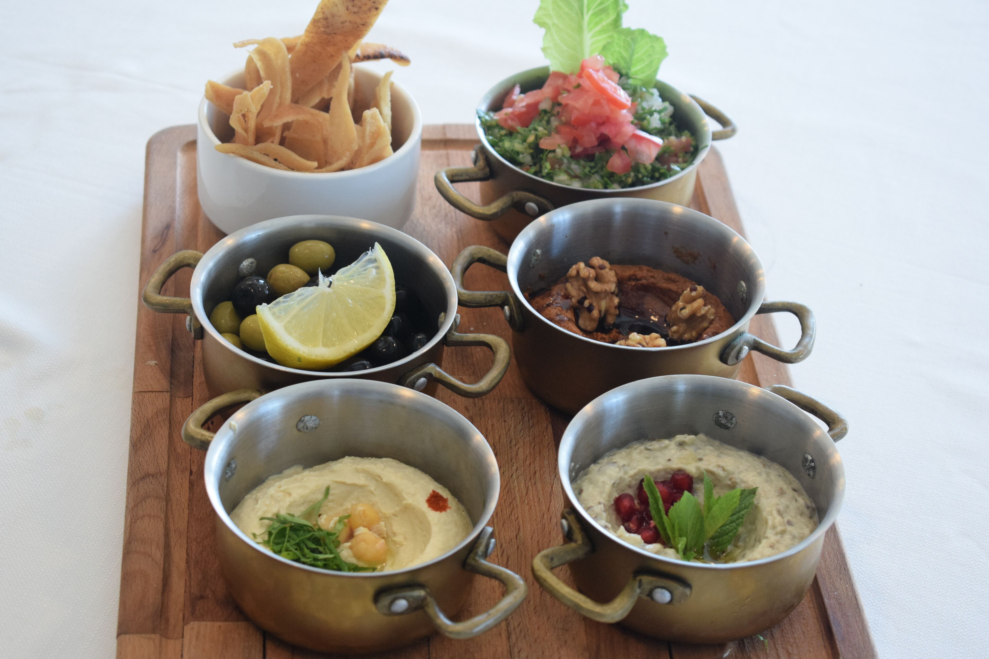 Una mesa de madera con varios platos, incluyendo aceitunas, hummus y una ensalada.