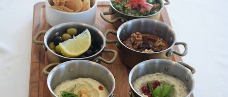 Una mesa de madera con varios platos, incluyendo aceitunas, hummus y una ensalada.