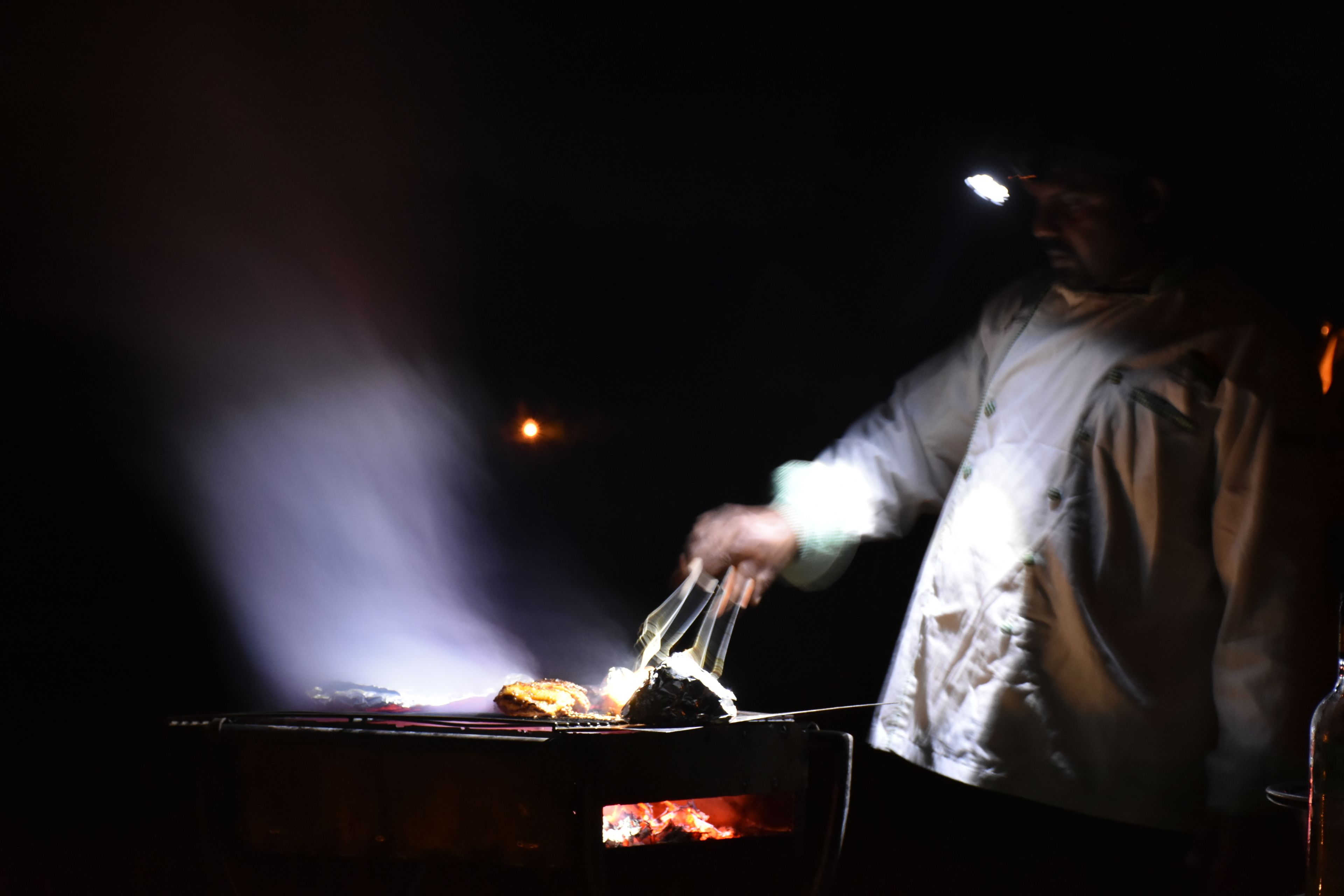 Une personne qui fait griller de la nourriture à l’extérieur, la nuit.