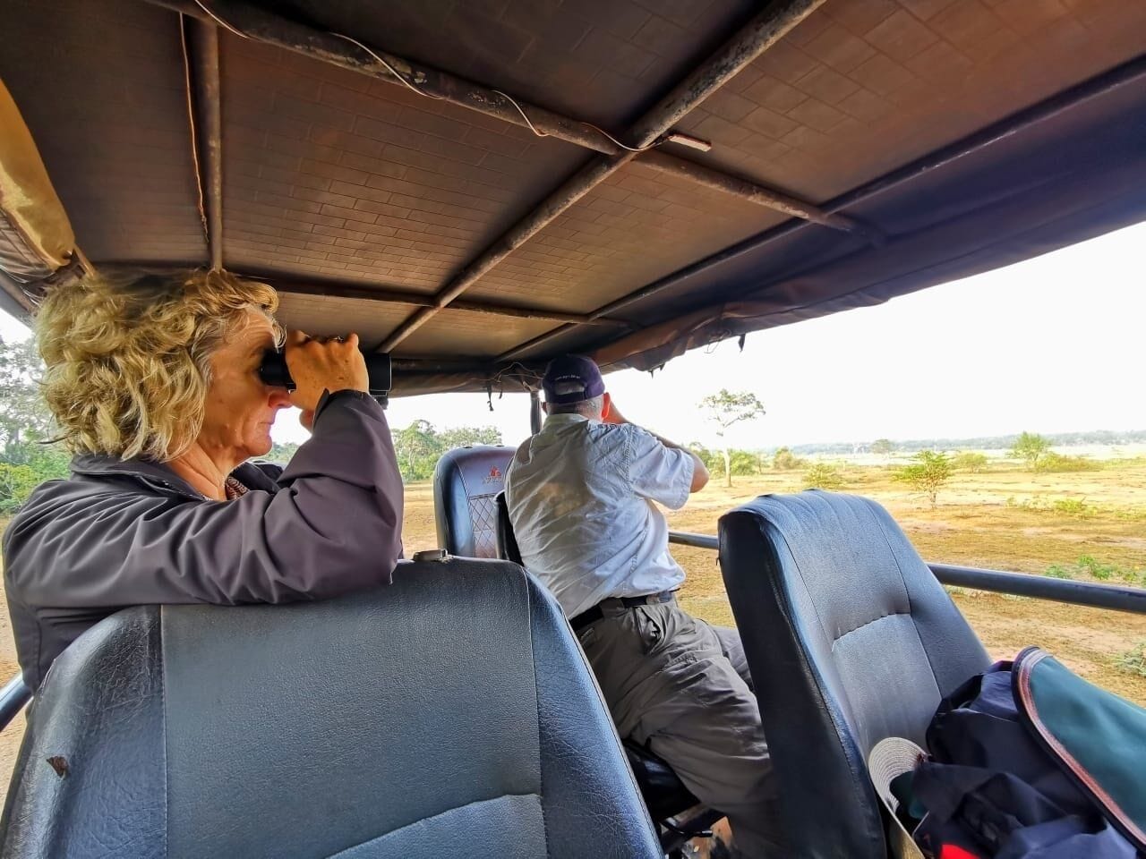 A vehicle interior with two seats, a metal roof, and a view of an open landscape.
