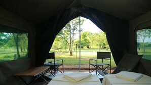 A tented room with two beds, a table, and two chairs, overlooking a grassy area with trees. - Big Game Yala by Eco Team (Kataragama)