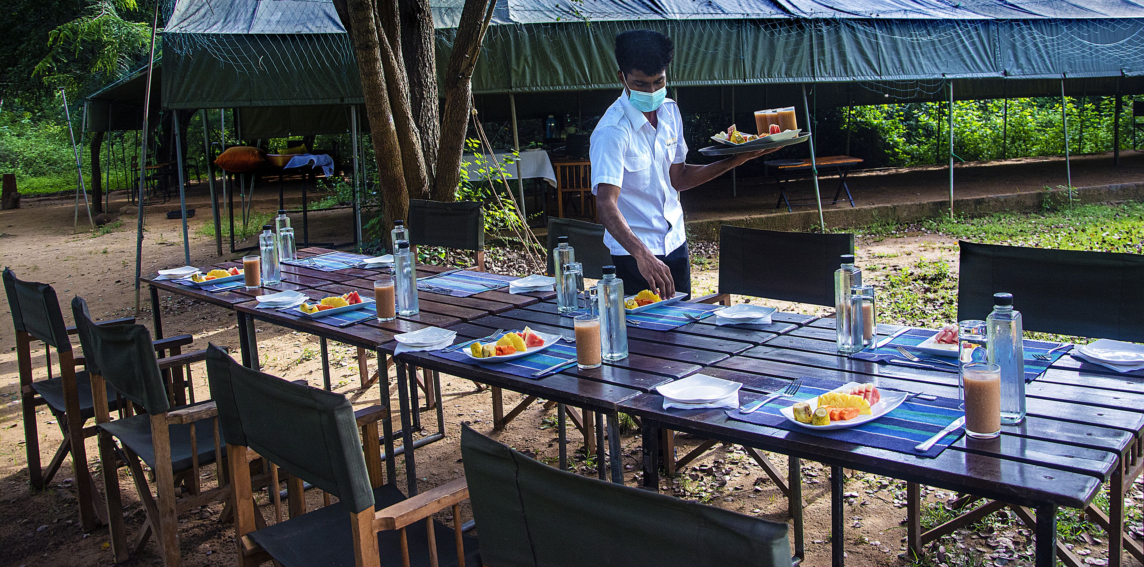 Un espace de restauration en plein air, avec des tables dressées pour les repas, entourées de chaises et de tentes.