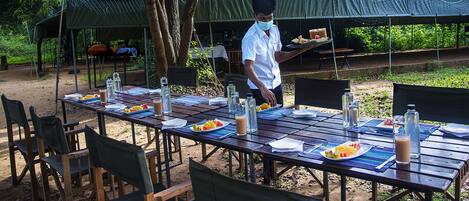 Un espace de restauration en plein air, avec des tables dressées pour les repas, entourées de chaises et de tentes.