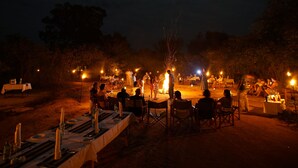 An outdoor dining area with tables set up for a meal, surrounded by trees and a campfire in the center. - Big Game Yala by Eco Team (Kataragama)