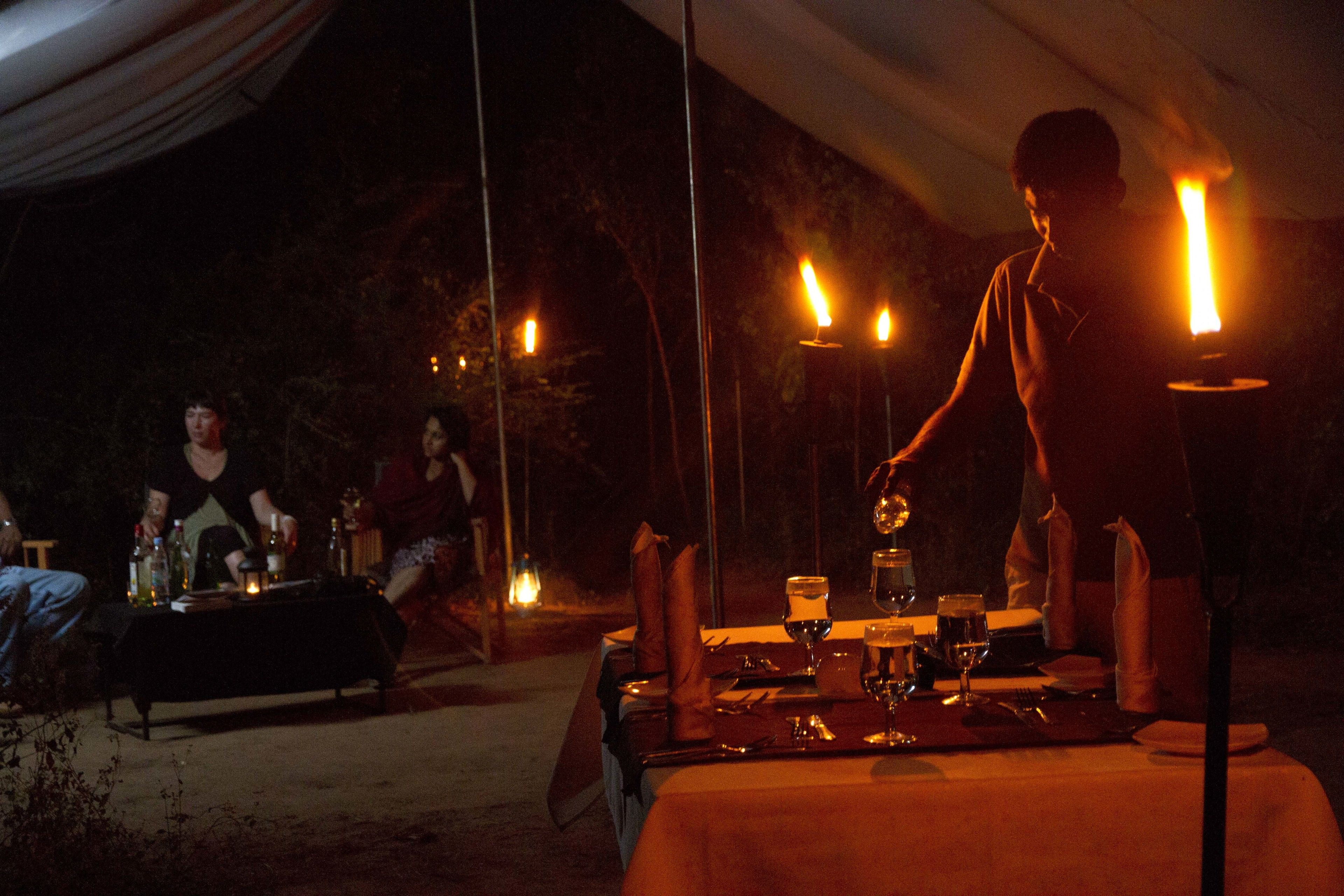 An outdoor dining setup with tables set for two, candles, and a person standing by the table.
